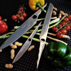 A collection of chef's knives with peppers, tomatoes, and peanuts on a black surface.