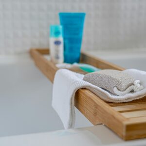 A relaxing bath setup featuring a wooden tray, pumice stone, towel, and skincare products.