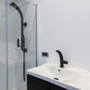 Modern minimalist style interior design of bathroom with white tiled walls and washbasin and black faucet and shower unit with glass partition