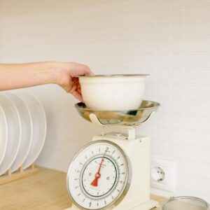 Close-up of hand placing a bowl on a kitchen weighing scale for food preparation.
